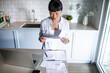 © Marko Geber - Woman reviewing household bills at kitchen counter