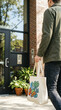 © pattaphorn - Person carrying reusable tote bag with vegetable prints approaches modern building entrance reflecting vibrant co living community culture