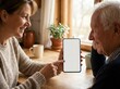 © Natalia Gotsyk - Adult woman showing mobile phone with blank mockup screen to elderly man at wooden kitchen table, helping senior with digital app.