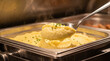 © INT888 - Close up of silver serving spoon scooping hot mashed potato from stainless steel buffet dish