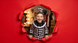 © ZaStock - Child dressed as jester peeking through torn red paper. Costume party, Halloween, children s entertainment, performance.