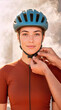 © pufanya - Vertical close up portrait of a smiling female cyclist wearing a copper brown jersey as hands adjust the strap of her teal helmet. Outdoor sports safety, preparation and teamwork concept
