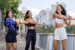 © ultramansk - A group of three Hispanic women in sportswear, concentrating on the stretch, follow the same stretch as a group with a sports jacket tied around the waist, outdoors in the city.