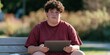 © Andrii Zastrozhnov - Teen boy in maroon t shirt sitting on park bench holding a tablet for study and casual browsing background for educational or lifestyle design