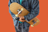 Young man with skateboard on orange background, closeup