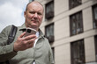 © svetlana_cherruty - Mature male freelancer using smartphone outdoors near modern residential building, contemporary remote work, mobile technology and urban lifestyle concept.