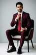 © miss irine - Young Indian businessman sits on modern chair wearing elegant maroon suit, red tie. Confident man poses for pro portrait in corporate style. Stylish male model shows successful entrepreneur look with