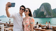© Viktor - Young couple takes selfie on cruise ship deck with island scenery. Smiling pair enjoys summer vacation, capturing moment together in warm weather.