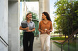 © pablo - Two businesswomen walking and conversing outdoors near an office building