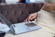 © waragron - A pregnant woman sits on a couch using a laptop, with one hand on her belly and the other navigating the touchpad.