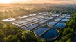 © CuteBee - Aerial view of industrial wastewater treatment plant with circular sedimentation tanks and water filtration systems surrounded by lush green forest landscape at sunrise light