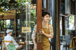© Rakchanok - Yong small business owner opening cafe door with open sign displayed, inviting customers inside cozy coffee shop and restaurant, daily startup routine reflecting growth and opportunity in business.