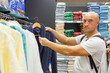 © Екатерина Переславце - Portrait of a bald caucasian man with blue eyes facing the camera while choosing a bathrobe in a home textile shop, useful for retail and customer trust content.