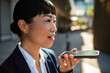 © Davor - Businesswoman using smartphone voice assistant on city street