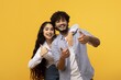 © Prostock-studio - Smiling Young Indian Couple Expressing Joy And Positivity With Thumbs Up Gesture, Standing Together In Photo Studio. Celebrating Happiness And Connection In A Bright Yellow Background.