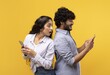 © Prostock-studio - Surprised Young Indian Couple Engaged With Their Smartphones, Showing Playful Emotion And Joy While Standing Back To Back At Studio Setting. Enjoying Technology Together. Business Concept.