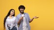 © Prostock-studio - Cheerful South Asian Woman And Man Smiling Together, Pointing At Empty Space In Bright Studio Setting. Perfect For Business Concept Or Advertising Use With Copy Space To Highlight Products.