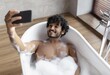 © Prostock-studio - Smiling Young Asian Man Taking Selfie With Smartphone While Enjoying A Relaxing Bath In Bathtub Full Of Bubbles, Sitting At Home. Personal Care And Wellness Concept.