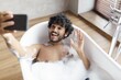 © Prostock-studio - Smiling Young Man Enjoying Relaxing Moment By Taking Selfie In Bathtub Filled With Bubbles At Home. Cheerful Mood In Modern Bathroom Setting. Wellness Concept.