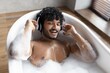 © Prostock-studio - Smiling Young South Asian Man Enjoying Relaxing Bath With Headphones, Surrounded By Foam, In Cozy Bathroom Setting, Indulging In Self-care Routine, Home Spa Concept.