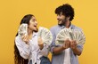 © Prostock-studio - Smiling Young Multiracial Couple Holding Cash While Looking At Each Other In Studio Setting. Happy Man And Woman Expressing Joy And Excitement With Money, Yellow Background. Wealth Concept.