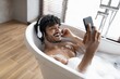 © Prostock-studio - Happy Young Man Enjoying Relaxing Bath With Bubbles And Listening To Music Through Headphones, While Holding Smartphone In Modern Bathroom. Home Spa Concept.