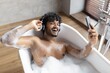 © Prostock-studio - Smiling South Asian Male Relaxing In Bathtub Full Of Bubbles, Listening To Music With Headphones. Enjoying Leisure Time In Bathroom, Indulging In Spa Experience. Spa Concept.
