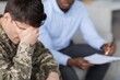 © Prostock-studio - Worried Young Caucasian Male Soldier In Military Uniform Covering His Face With Hand During Therapy Session In Office Setting, Receiving Support From Therapist. Healthcare Concept.