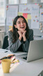 © pattozher - Joyful Woman in Office: A young woman with a bright smile beams with happiness while working at her desk, surrounded by office supplies and a laptop.