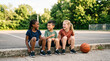 © crylines - Group of diverse young children sitting together on a basketball court laughing.