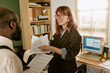 © AnnaStills - Diverse young adult colleagues discussing paperwork in retro style office. Caucasian woman pointing at document while talking to African American man, suitable for corporate training