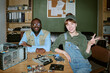 © AnnaStills - Portrait of diverse young adult colleagues smiling at desk with disassembled computer parts in retro office. Image represents tech support and hardware repair services