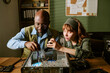 © AnnaStills - Middle aged African American man and young adult Caucasian woman repairing computer in retro office. Image represents teamwork and technical support for hardware maintenance campaigns