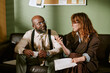 © AnnaStills - Middle aged African American man and Caucasian woman in retro office discussing documents during business meeting. Image suitable for corporate communication and vintage workplace marketing