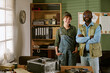© AnnaStills - Portrait of diverse young adult Caucasian woman and middle aged African American man smiling in retro repair shop. Image represents teamwork and is ideal for tech service marketing