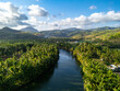 © Amazing Aerial - Aerial view of a river winding through a dense palm tree forest with rolling mountains in the background under a bright sky in Pacitan, East Java, Indonesia.