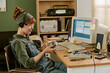 © AnnaStills - Young adult Caucasian woman wearing headphones and holding portable CD player in retro office. Image represents vintage technology and is suitable for nostalgic marketing campaigns