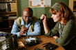 © AnnaStills - Diverse middle aged colleagues repairing computer hardware in retro office, African American man using screwdriver while Caucasian woman holds flashlight, ideal for tech support marketing