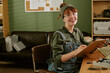 © AnnaStills - Portrait of smiling young adult Caucasian woman technician writing on clipboard in retro office. Image represents vintage engineering and is suitable for technical education marketing