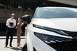 © wedmoments.stock - Car dealer discussing a new modern vehicle with a businesswoman at an outdoor dealership. Concept car purchase, professional service and modern mobility.