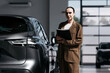 © wedmoments.stock - Female car dealer with a tablet standing beside a new vehicle. Concept automotive business, customer consultation and car sales.