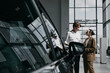 © wedmoments.stock - Car dealer advising a woman beside a modern vehicle. Concept car sales, customer service and vehicle selection.