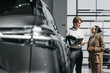 © wedmoments.stock - Salesperson consulting a female customer beside a new car in a modern showroom. Concept vehicle selection, purchase and customer service.