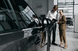 © wedmoments.stock - Car dealership consultant discussing a new vehicle with a female customer in a modern showroom. Concept car purchase and professional service.