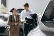 © wedmoments.stock - Stylish new vehicle in a showroom with buyers considering their purchase. Concept car sales and dealership business.