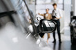 © wedmoments.stock - Woman talking with a salesperson beside a modern car while choosing a vehicle in a dealership.