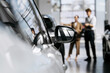 © wedmoments.stock - Woman and automotive consultant discussing a new car beside the vehicle in a bright showroom.