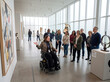 © Syifa - Female museum docent in a wheelchair leading a guided tour of a modern art gallery for visitors