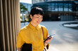 © Davor - Smiling businesswoman using smartphone outdoors in modern city