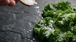 © Freyaundiclosed - Hand sprinkling sea salt over fresh kale leaves on a dark stone surface